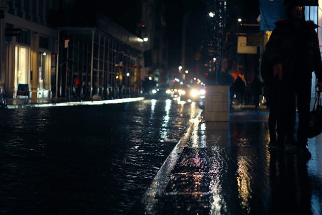 Urban city street on a rainy evening with pedestrians and reflections on wet pavement